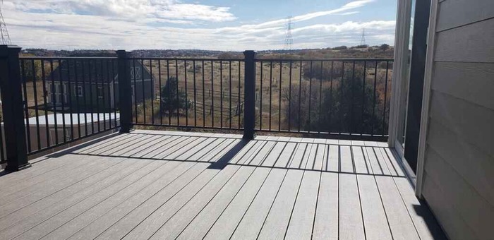 A deck with a black railing and a view of a field.