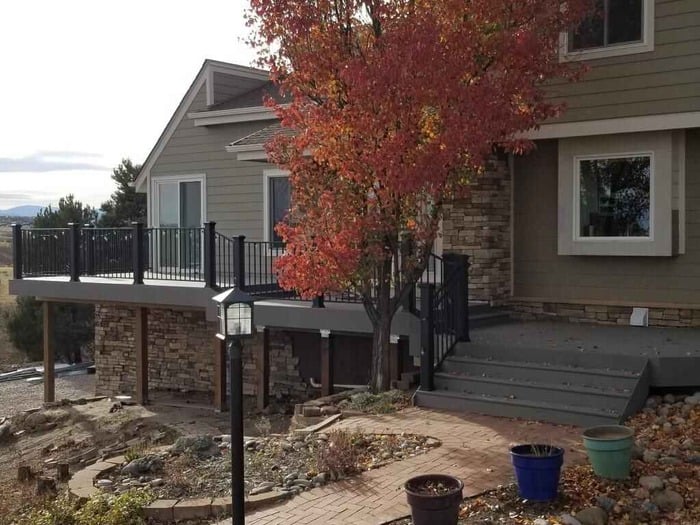 A house with a deck and a tree in the front yard.